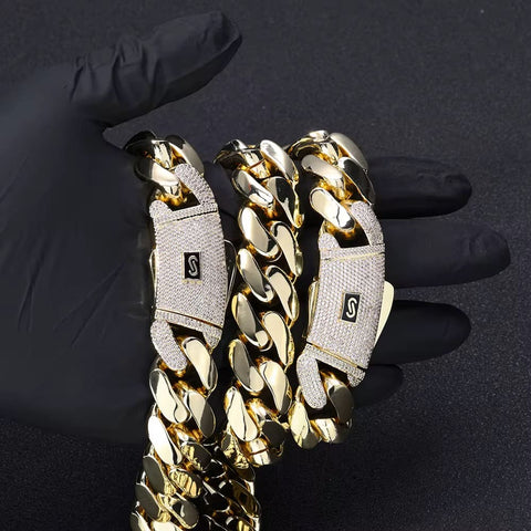 Gold chain bracelet with diamond-encrusted clasp held by a gloved hand on a dark background

